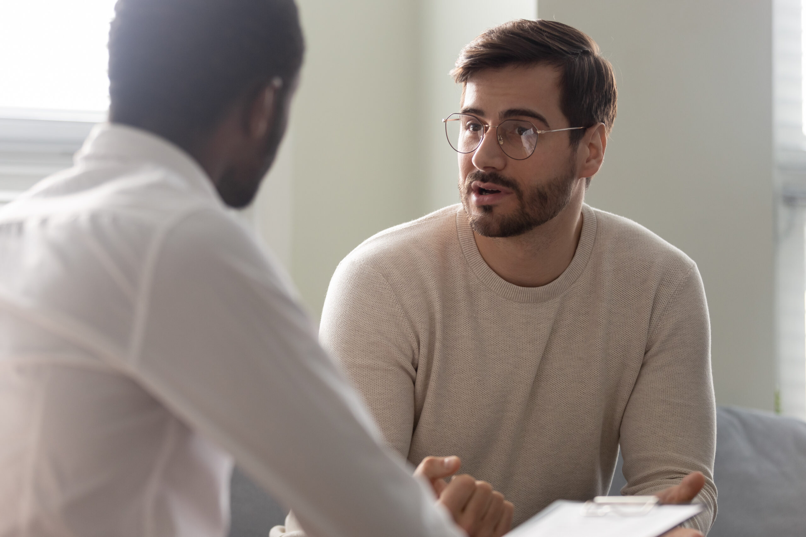 Man,Consulting,With,Practitioner,,African,Psychologist,Holding,Clipboard,With,Card